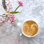 A latte next to a vase of flowers